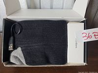 Black heated socks folded in a black box with USB wired connection and white rechargeable battery box visible