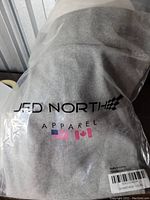 Front view of grey Jed North apparel item inside plastic packaging showing brand logo and flags.