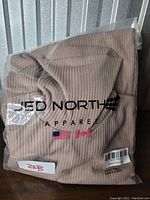 Tan ribbed hoodie from JED NORTH Apparel, still sealed in plastic packaging showing brand and flags.