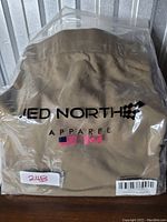 Packaged khaki Jed North hoodie with brand logo and flags visible on plastic packaging.