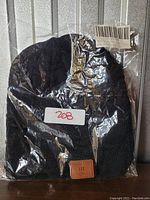 Black knit beanie hat in clear plastic packaging, showing a brown patch with an embossed music equalizer design.