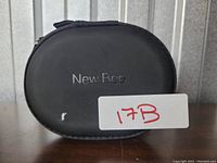 Closed black oval-shaped zippered carrying case with New Bee logo.