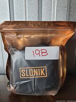 Slonik branded sealed pouch containing the headlamp and accessories, labeled 19B.