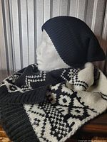 Mannequin head wearing a black knit slouchy winter hat paired with a black and white knit scarf with a geometric pattern.