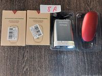 Two boxed rechargeable hand warmers, a silver hand warmer in plastic casing, and a red hand warmer device with USB cable on wooden surface.