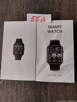 Front view of two smart watch boxes showing images of the watches, one with a colorful fitness tracking display and the other with a digital fitness tracker screen.