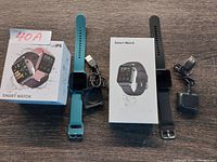 Two smart watches displayed with their charging cables and original boxes on a wooden surface.