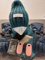 Knitted dark green ribbed hat, matching scarf in green, brown, cream, blue heated gloves, and two coral rechargeable hand warmers on display.