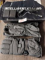 Photo shows a pair of black intelligent heated gloves with adjustable strap and power button, two rectangular battery packs, and a car USB adapter, all placed on a black cloth with the words INTELLIGENT HEATING.