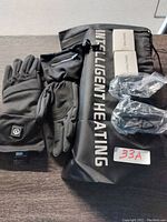 Photo of the black intelligent heated gloves, black drawstring bag with 'Intelligent Heating' text, two batteries, and charging cables