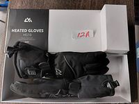 Top-down view of black heated gloves HG10 in white branded box with product label and model number visible.