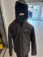 Front view of heated jacket with hood and visible control buttons on chest area.
