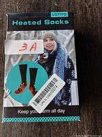 Front of box showing brand I.O.TIYO and heated socks in packaging with image of woman dressed in winter clothes.