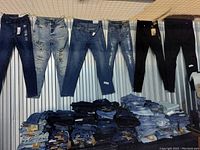 Photo of jeans displayed hanging on a wall and stacked in piles below, showing a variety of styles and washes