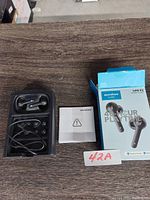 Soundcore Life P2 wireless earbuds in black with charging case in black plastic tray, user manual, and product box visible on wooden surface.