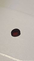 Oval faceted cherry red garnet on white background, top-down view.