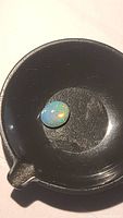 Oval cabochon Ethiopian opal gemstone resting in a black dish, showing vibrant color play with green, orange and yellow flashes.