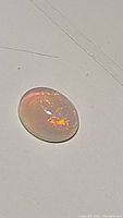 Close-up image of oval cabochon cut Ethiopian opal with orange and fiery rainbow play-of-color visible.