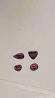 Four loose rubies on white background—pear, trillion, round, oval shapes visible