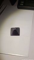 Top view of a hand carved dark purple amethyst pyramid on white surface showing square base and polished facets.