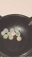 View of 11 small round natural Ethiopian opals with a milky body color and rainbow flashes in a container.