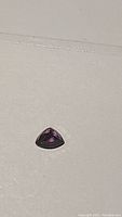 Close-up photo of a single trillion cut sapphire gemstone with deep red purple pinkish color on a white background.