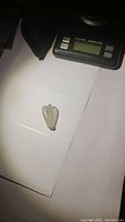 Photo of the carved crystal quartz angel on a white paper background next to a digital scale.