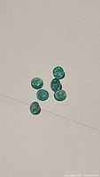 Six round natural emerald gemstones displayed together on a flat surface showing their green color and clarity.