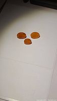 Three oval cut natural orange carnelian gemstones placed on a white surface, showing their color and size variation.