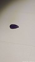 Photo of a deep purple pear cut amethyst gemstone showing the size and shape.