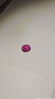 Close-up photo of the oval cut deep pink-red ruby gemstone showing its color, cut, and surface clarity.