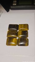 Six polished rectangular tiger's eye cabochons arranged on a white background showing chatoyancy and coloration.