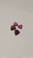 Four trillion cut rhodolite garnet stones displayed on white background, showing color and cut.