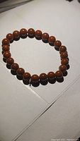 Red jasper stretchy bracelet laid flat showing round reddish-brown beads with polished finish and elastic cord.