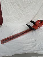 Full view of the Black and Decker electric hedge trimmer with orange body and black handle, blade covered in red protective sheath.