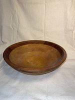 Front angled view of the Crate and Barrel oiled wood salad bowl on a light fabric background showing the inside curve and wood grain.