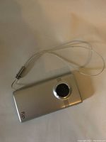 Silver Flip Video Camera with wrist strap facing front showing lens and speaker grills