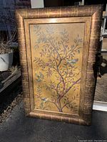 Full view of framed artwork showing tree branches with birds and fruit against a gold background. The frame is textured and brown with a goldish finish.