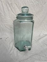 Clear hexagonal glass beverage dispenser with a matching lid and a silver spigot at the base, photographed from front-on view.