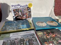 Five boxed jigsaw puzzles arranged side by side showing puzzle images on the boxes and some text.