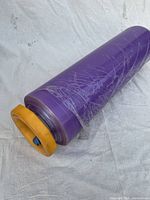 Close-up angled view of one roll of purple heavy duty plastic wrap with yellow-orange end cap holder.