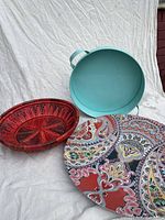 Photo showing three trays: red raffia basket, aqua aluminum tray with handles, and a large colorful melamine platter with paisley design.