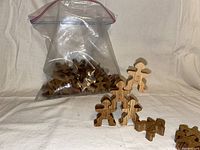 Wooden people-shaped stacking blocks arranged next to a zip-lock plastic bag containing the remaining blocks on a fabric background.