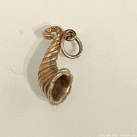 Clear top-down photo of the gold horn of plenty charm showing its curled, ribbed texture and attached jump ring.