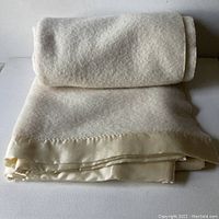 Folded cream wool blanket showing texture and satin trim edge.