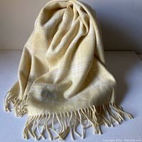 Light yellow wool scarf or throw with fringed ends arranged in soft folds on a white surface.