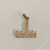 View of the front of a small 10K gold Parliament Hill charm showing textured design representing the building.