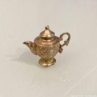 Front view of the vintage 10K gold urn charm showing detailed pattern work, spout, lid with finial, and handle.