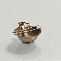 Front angle showing gold rice bowl charm with chopsticks crossing the top and spoon inside