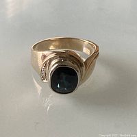 Front view on reflective surface showing cushion-shaped blue sapphire and offset diamond shoulders